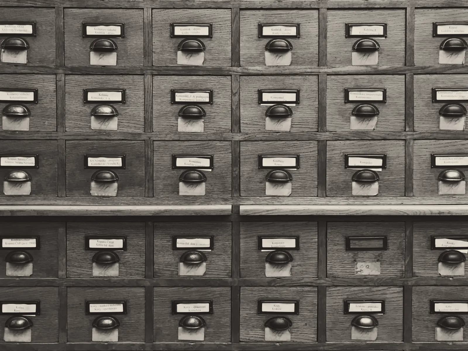 The wooden drawers of a card catalogue, in black and white.