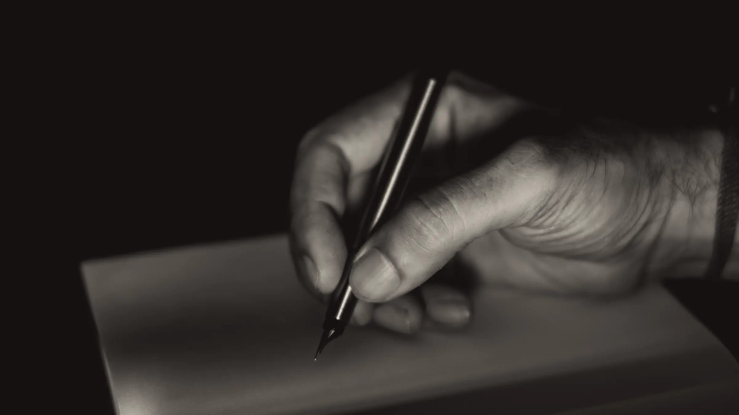 A hand writing with a fountain pen, in black and white.